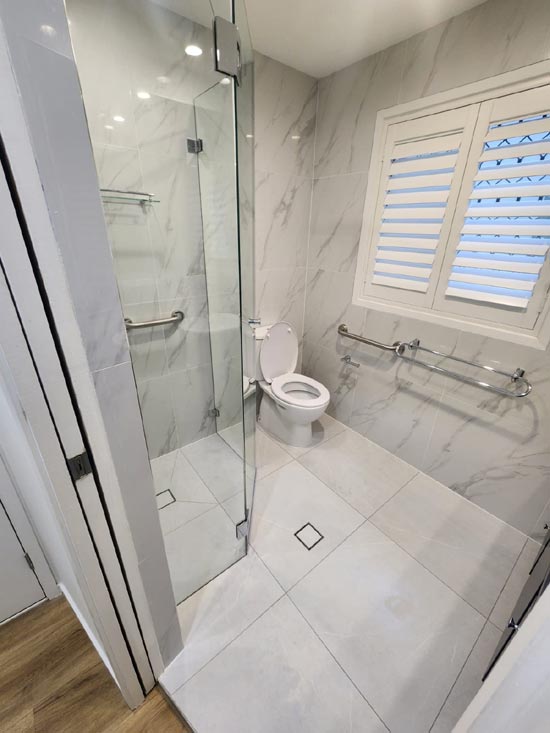 Completed bathroom with full marble tiling and a frameless shower screen